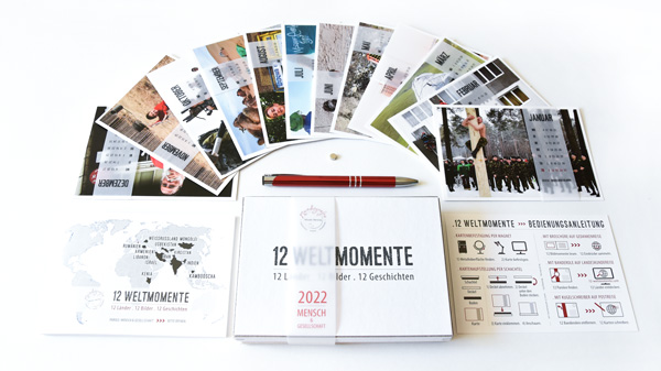 12 Weltmomente Schachtel mit Postkarten, Broschüre Bedienungsanleitung, Kugelschreiber, Minimagnet, Kalender und Onlineparolen